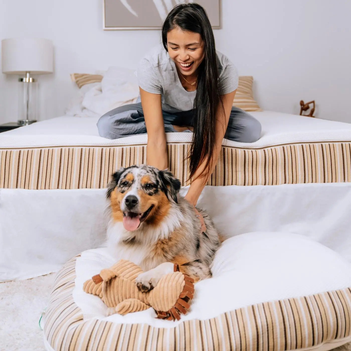 Girl sitting on Essentia Classic REM5 mattress petting her dog who is on the floor on his kingston organic pet bed