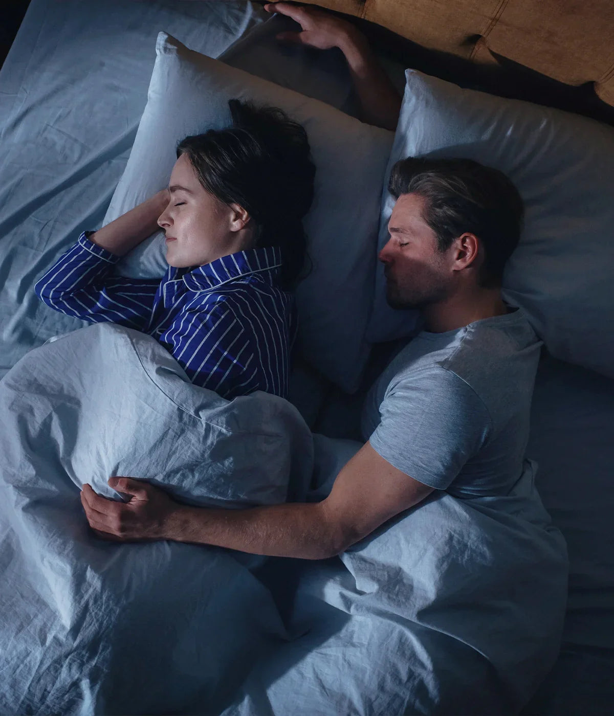 Husband wearing a grey t-shirt sleeping next to his wife wearing a dark blue striped pjs while comfortably dozing on an Essentia Venti double sided organic latex mattress.